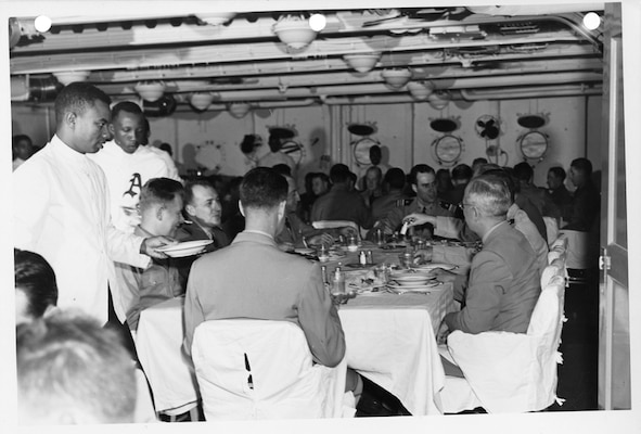 President Harry S. Truman (right foreground) dines with an unidentified group of sailors and officers on board USS Augusta. Note the two Black mess attendants serving the table while other Black attendants stand around perimeter of the wardroom look on.