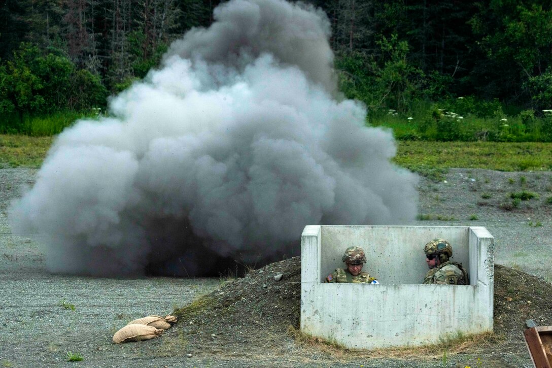 Two soldiers sit inside a shelter as a explosive detonates behind them.