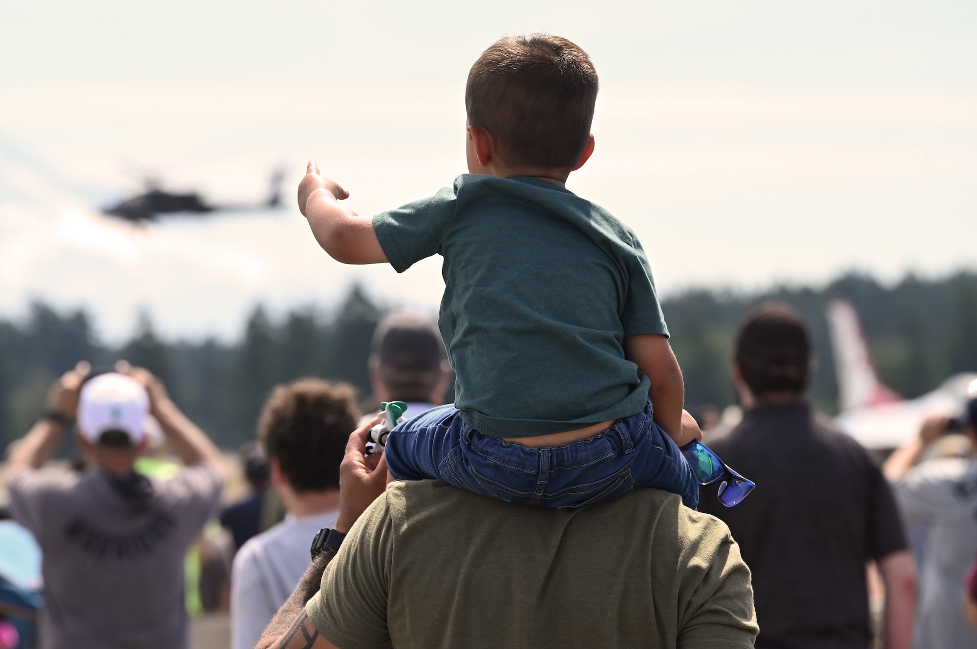 A young spectator points to a U.S. Army helicopter in the distance above the McChord Field flightline during the Joint Base Lewis-McChord Airshow and Warrior Expo at JBLM, Washington, July 16, 2023. The mission of the JAWE was to foster goodwill to educate and familiarize attendees with the people, mission, and equipment of the Air Force, Army, and other Armed Services while continuing to provide installation-wide mission support. (U.S. Air Force photo by Senior Airman Colleen Anthony)