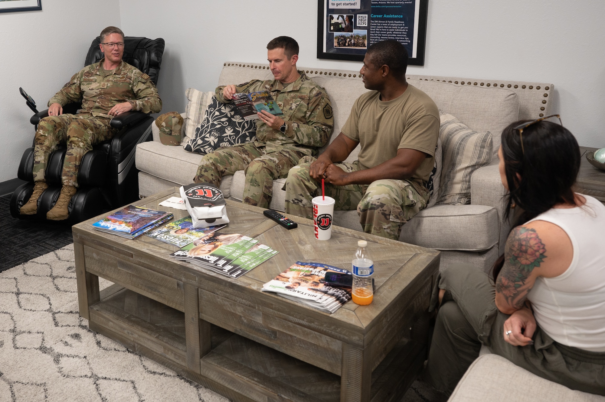 U.S. Air Force Chief Master Sgt. Michael Becker, 355th Wing command chief, sitting in a massage chair on the left, and Col. Scott Mills, 355th Wing commander, sitting on a sofa to the right of Becker, visit the welcome center at Davis-Monthan Air Force Base, Ariz., July 18, 2023. Two members of the welcome center team are seated to the right of Mills. The command team regularly met with units and organizations on base to connect with them. (U.S. Air Force photo by Airman 1st Class Jasmyne Bridgers-Matos)