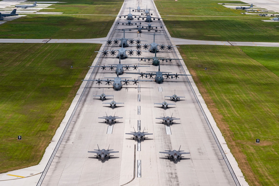 Small and large aircraft move in formation on a tarmac as seen from above.
