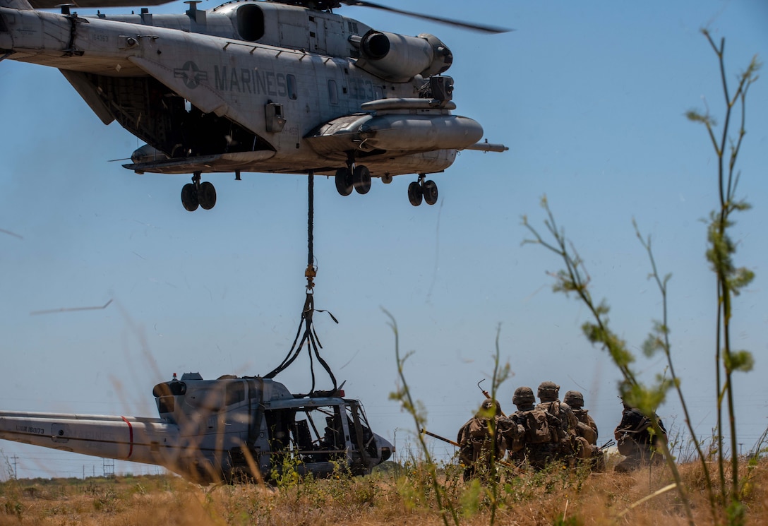 U.S. Marines assigned to Combat Logistics Battalion 15, 15th Marine Expeditionary Unit, observe a CH-53E Super Stallion attached to Marine Medium Tiltrotor Squadron (VMM) 165 (Reinforced), 15th MEU, externally lift a simulated down aircraft during tactical recovery of aircraft and personnel training at Marine Corps Base Camp Pendleton, California, June 30, 2023. The training, part of the I Marine Expeditionary Force Expeditionary Operations Training Group TRAP course, develops the capabilities of the TRAP force to enhance their capabilities recover aircraft, personnel, and equipment in austere environments. (U.S. Marine Corps photo by Lance Cpl. Kahle)