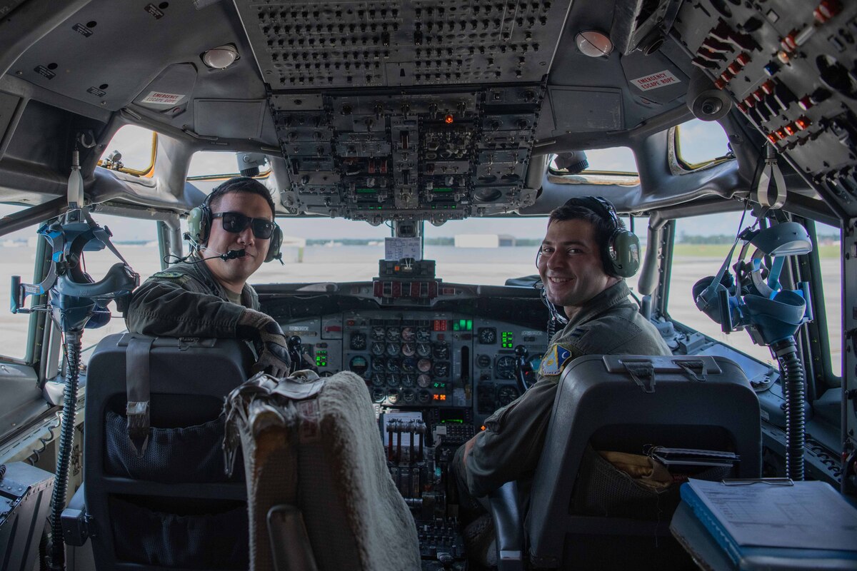 Two pilots smiling at the camera while sitting in a cockpit