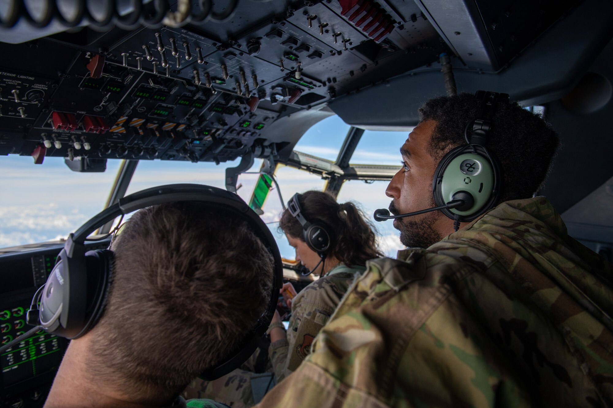 Airmen monitor the overhead panel in the flight deck of a C-130J