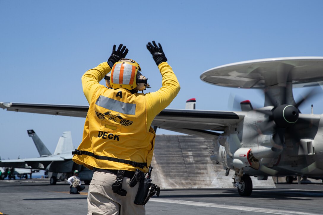 A sailor guides an aircraft on the  deck of a ship.