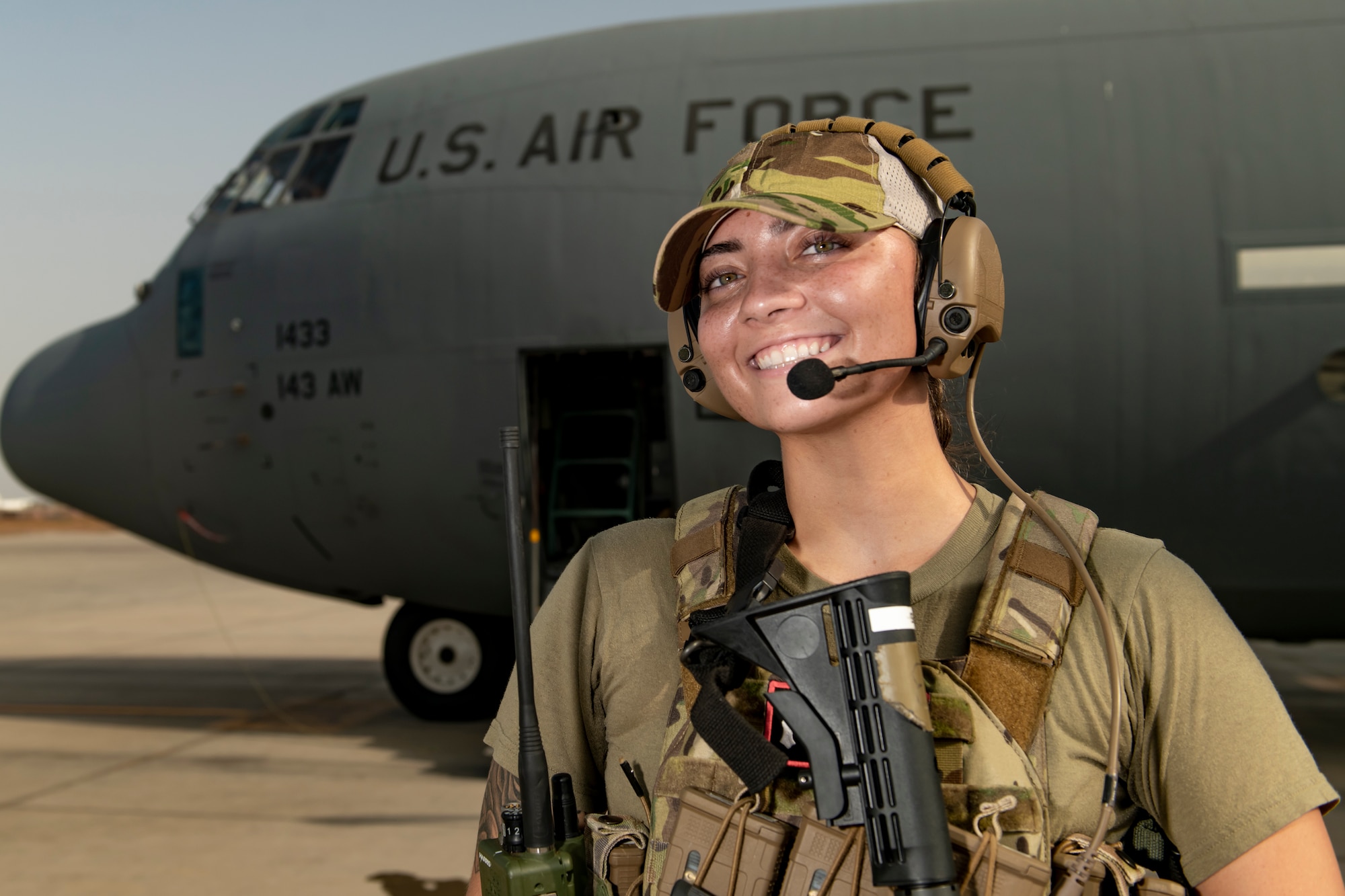 Photo of a woman in a bulletproof vest and holding a rifle in front of an airplane