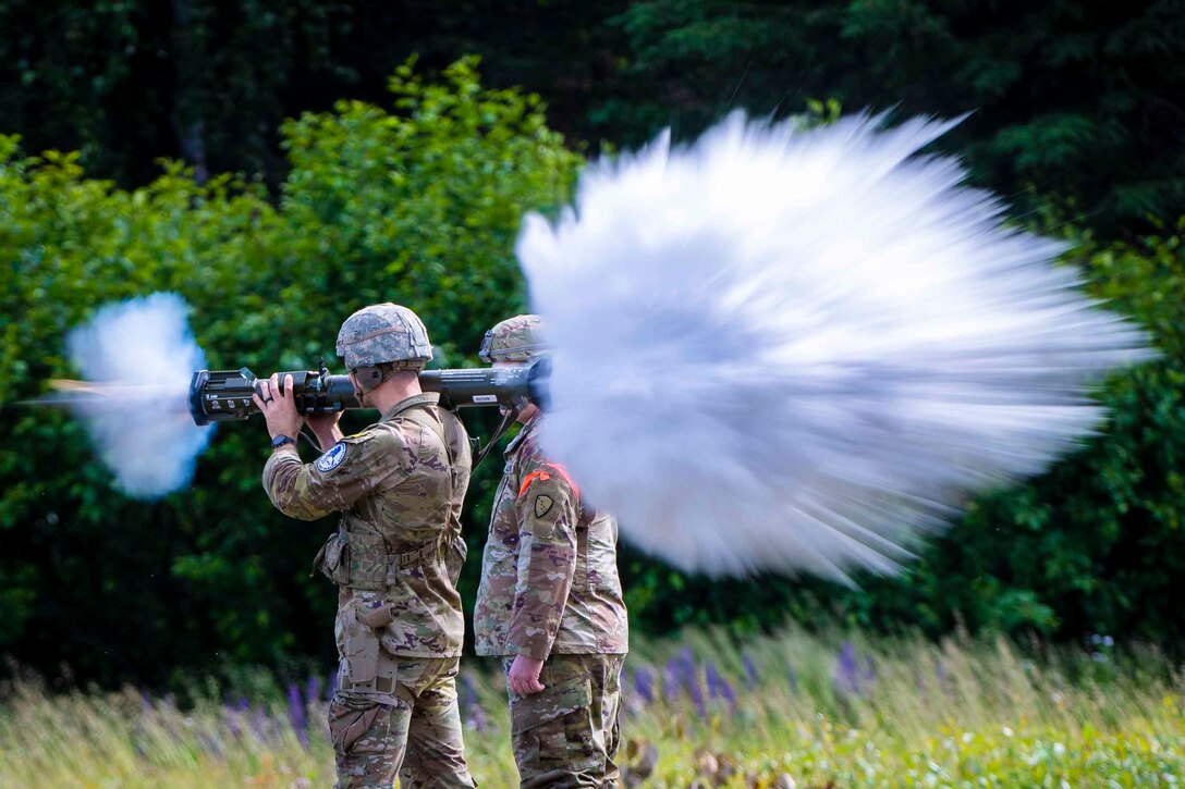 A soldier fires a weapon over his shoulder as another soldiers stands next to him.