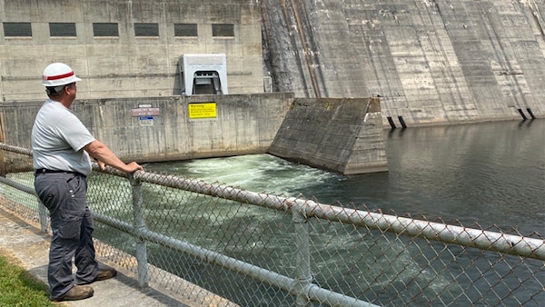 A man stands overlooking the tailwater at a dam