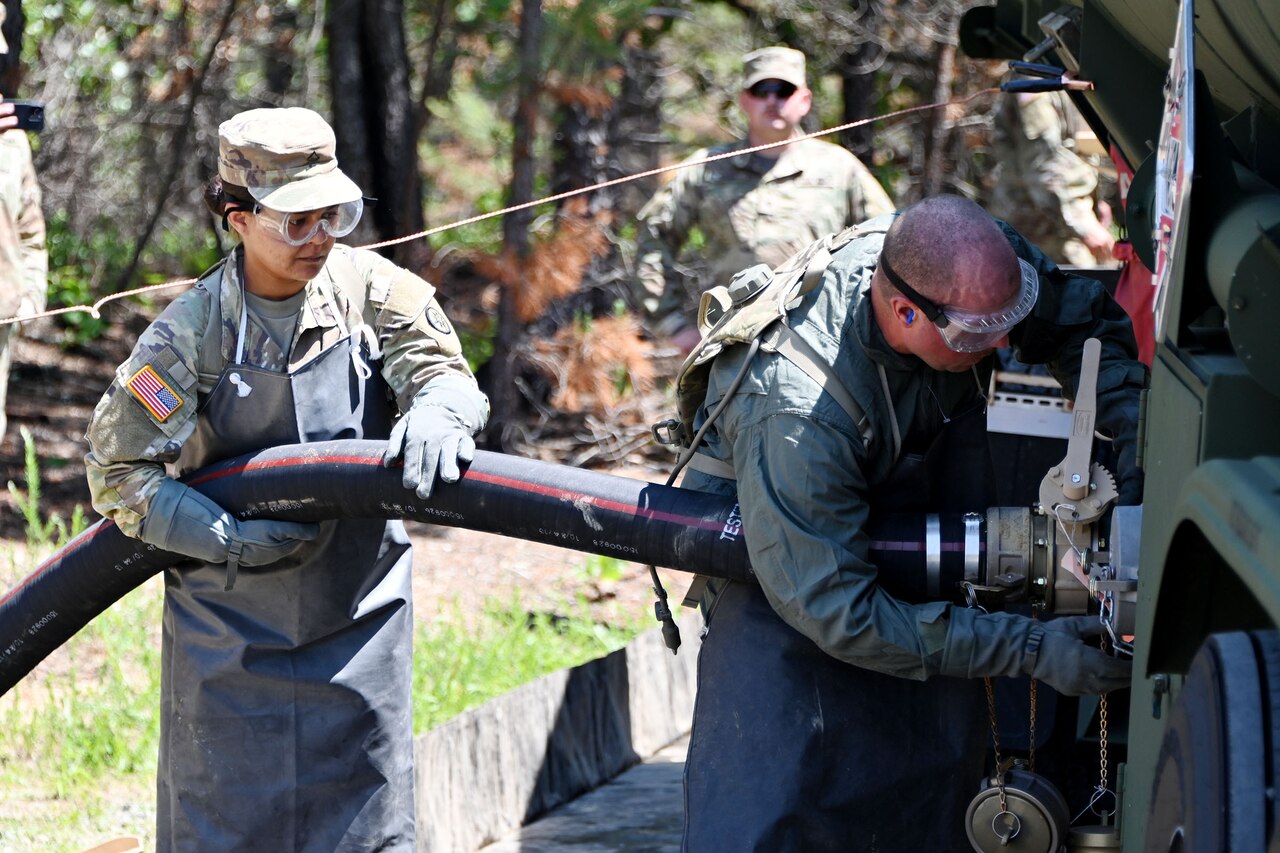 Two uniformed service member connect a hose to a military fuel truck.