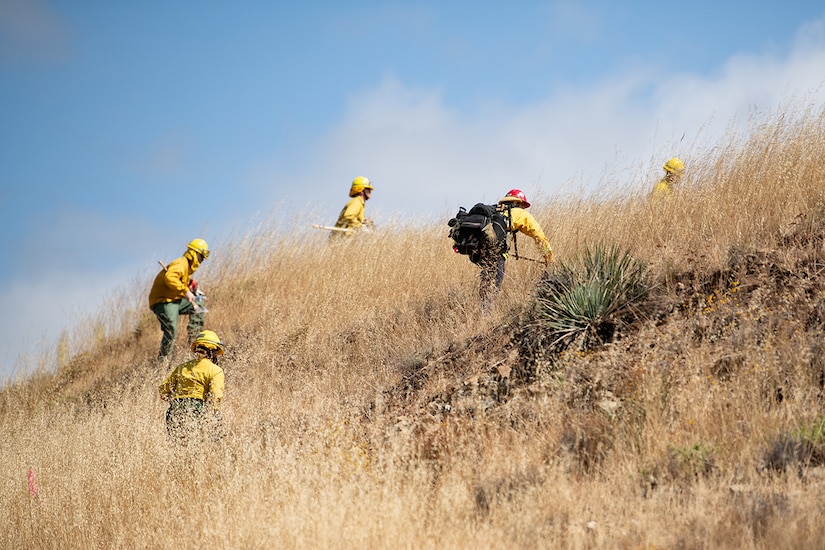 Service members wearing fire protection clothing run up a hill.
