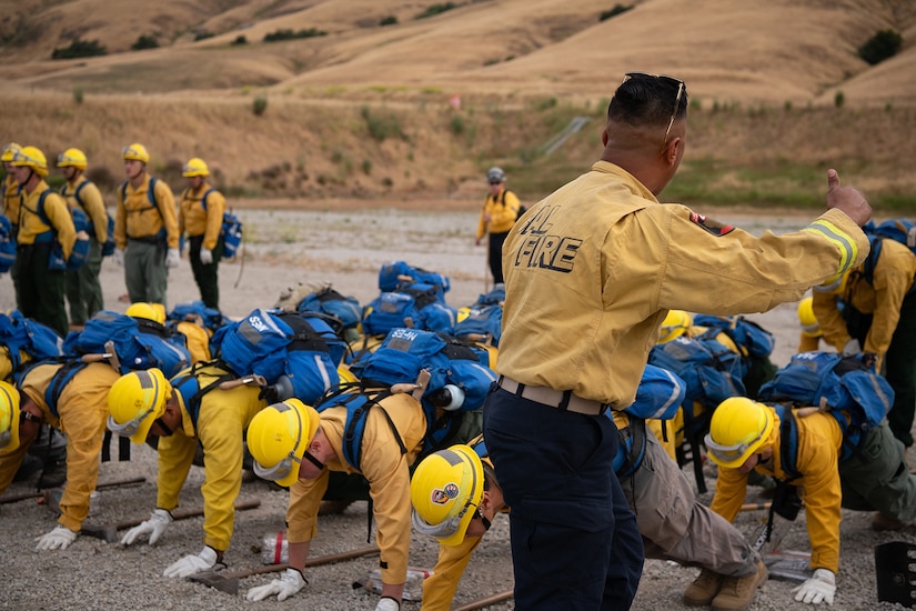 Service members wearing fire protection clothing do pushups while in formation.