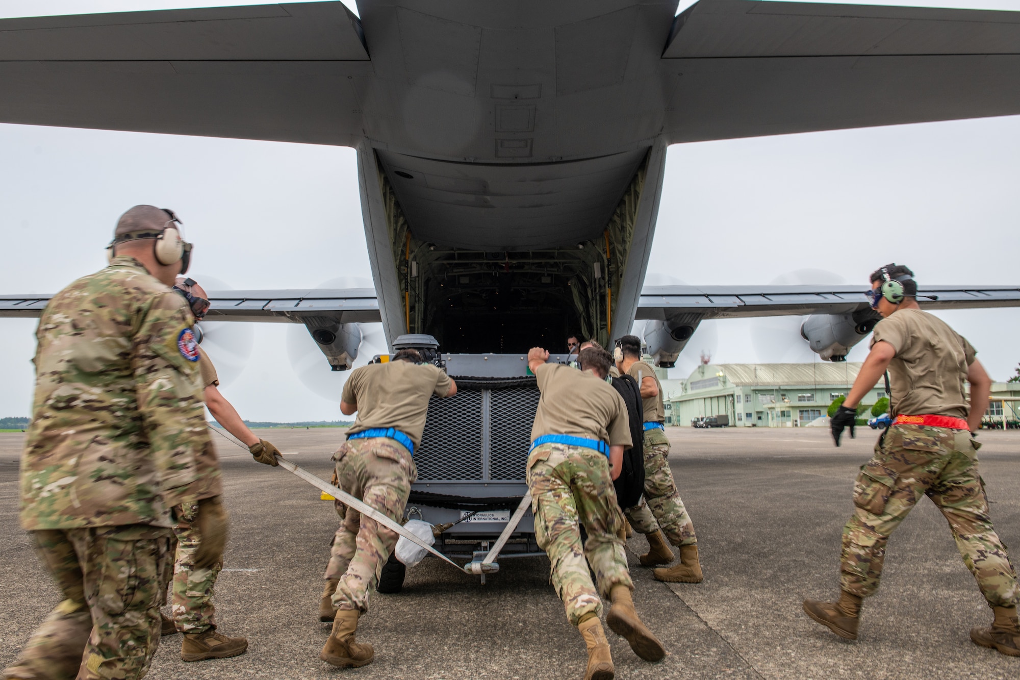 Airmen work together to move a mobile air conditioner onto a C-130J