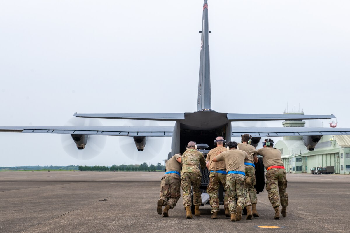 Airmen work together to move a mobile air conditioner onto a C-130J