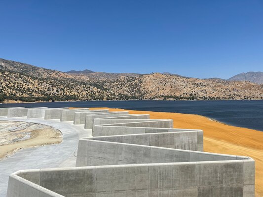 a labyrinth weir in the foreground with a lake and mountains in the background