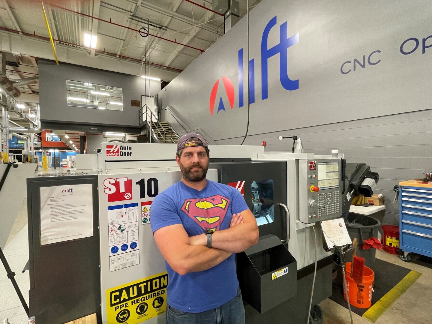 An Operation Next Success Story: Staff Sgt. Cameron Homburg, a student enrolled in LIFT’s Operation Next program, poses for a photo in front of CNC machining. Homburg is more than halfway through four CNC certification he hopes to earn through Operation Next; CNC Lathe, CNC Mill, Safety, and Floor Operations.