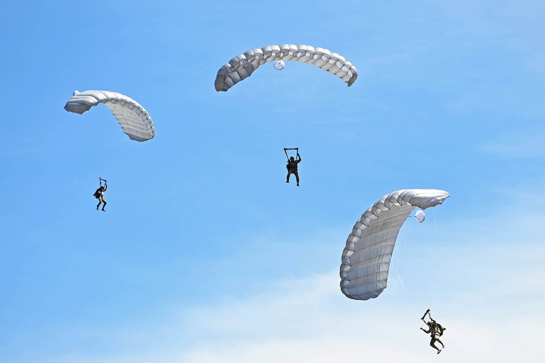 Three airmen wearing parachutes participate in a daylight free-fall jump during an airshow.