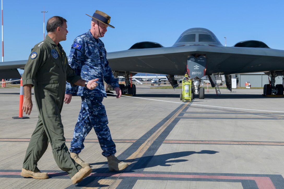 Two men in military uniform walk in front of a military aircraft.
