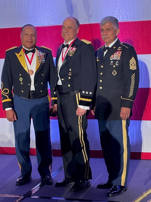 three men stand on a stage while wearing formal attire