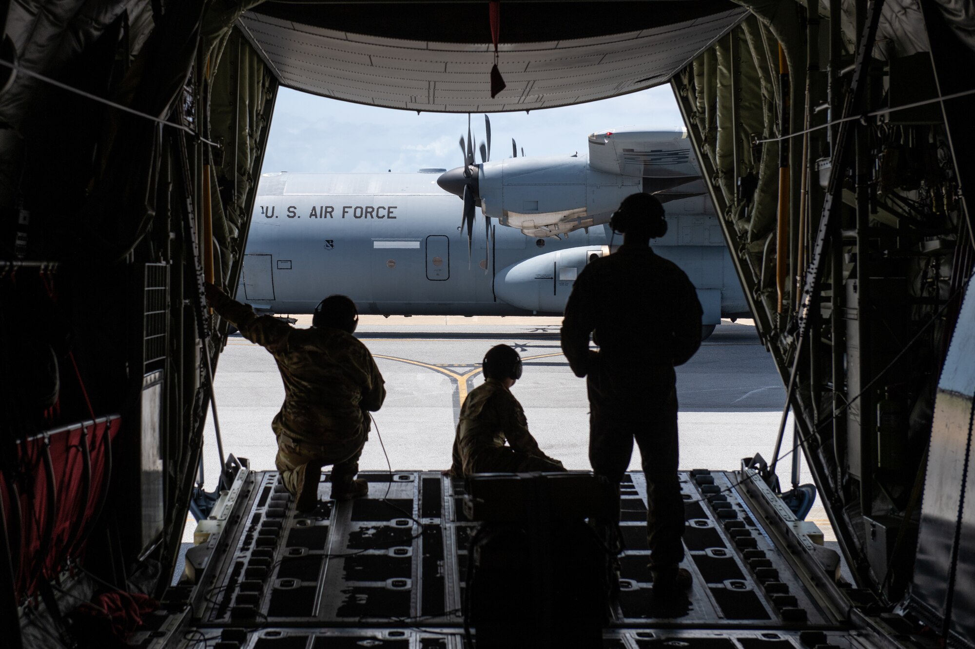 Airmen watch from the ramp of a C-130J Super Hercules as another C-130J taxis across the flightline