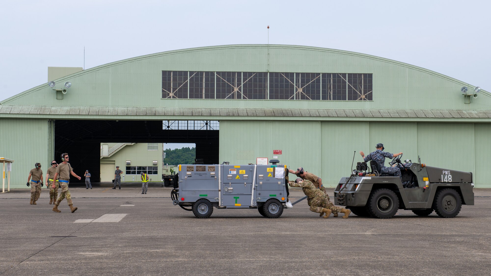 Airmen work together to move a mobile air conditioner across a flightline