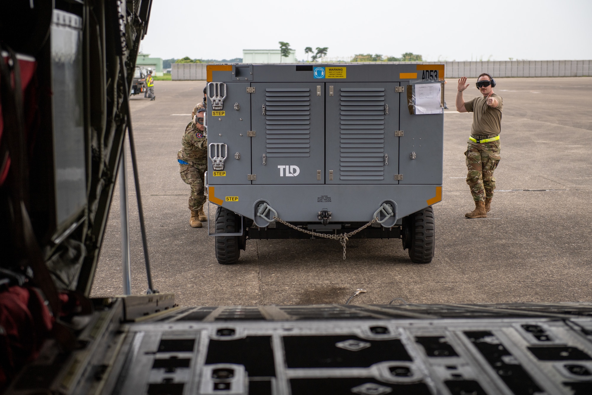 Airmen guide a mobile air conditioner onto a C-130J