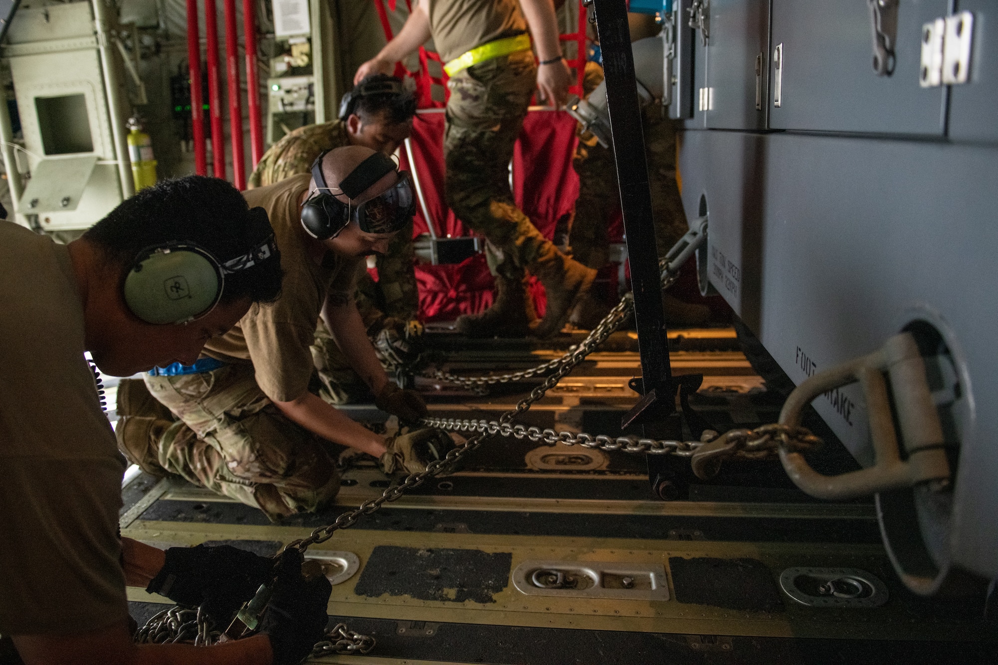 Airmen tie down a mobile air conditioner aboard a C-130J