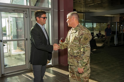 A man wearing business attire shakes hands with a uniformed service member inside a building.