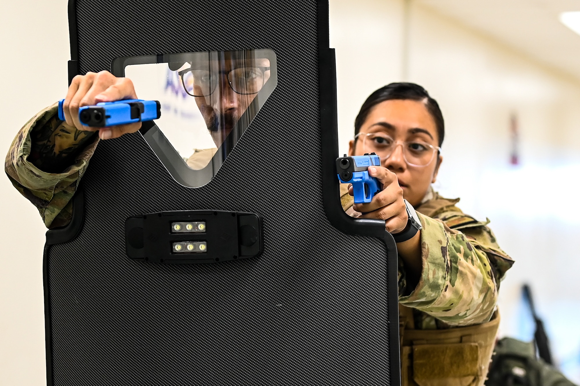 U.S. Air Force Staff Sgt. Anthony Zayas (left), 47th Security Forces Squadron flight sergeant, and Staff Sgt. Siree Mooney (right), 47th SFS flight sergeant, aim down sights behind a ballistic shield during a training exercise created by the Val Verde Sheriff's Office at San Felipe Memorial Middle School, Texas, July 12, 2023.