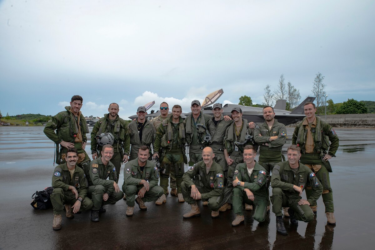 Pilots assemble for a group photo in front of an aircraft.