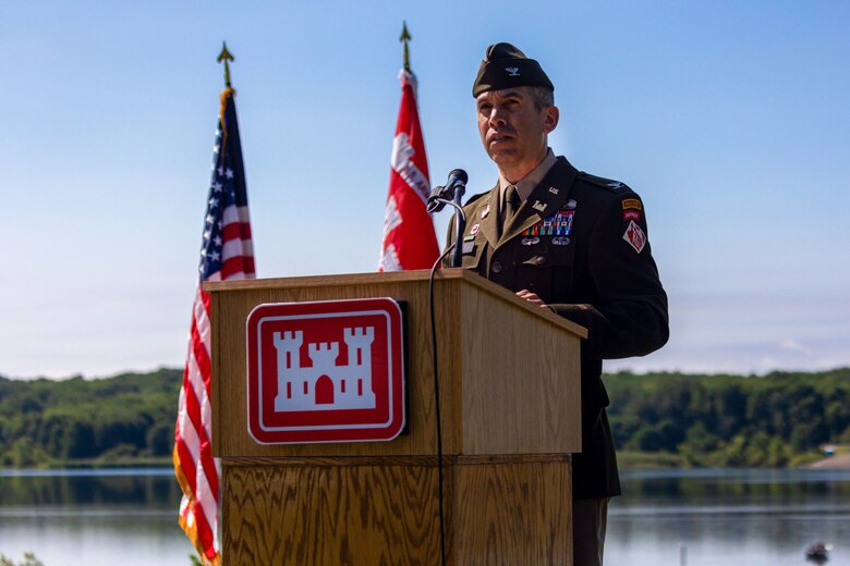 A man speaks at a podium in front of a lake.