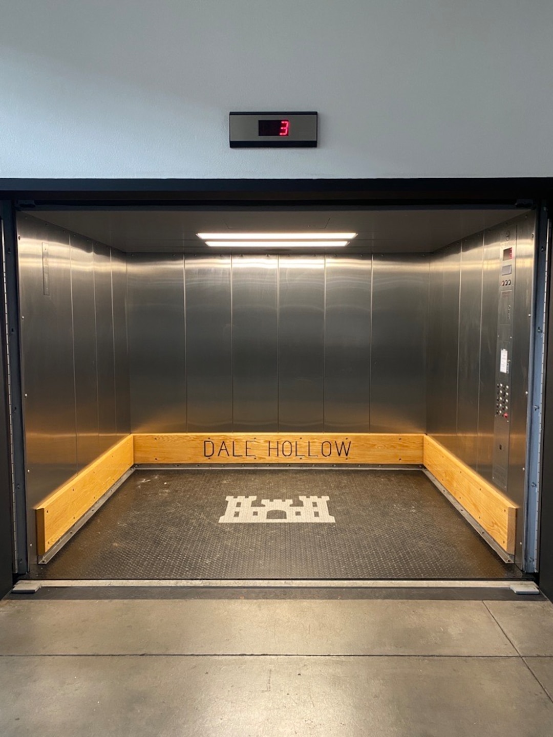 An elevator car shaft has custom wood framing with Dale Hollow burned in and a Corps Castle logo on the floor of the car.
