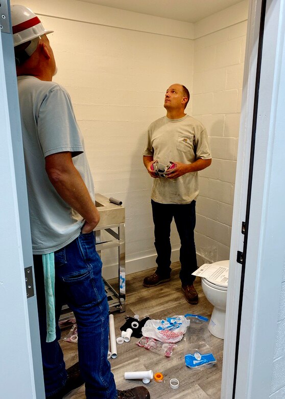 Two men stand inside a newly constructed bathroom.