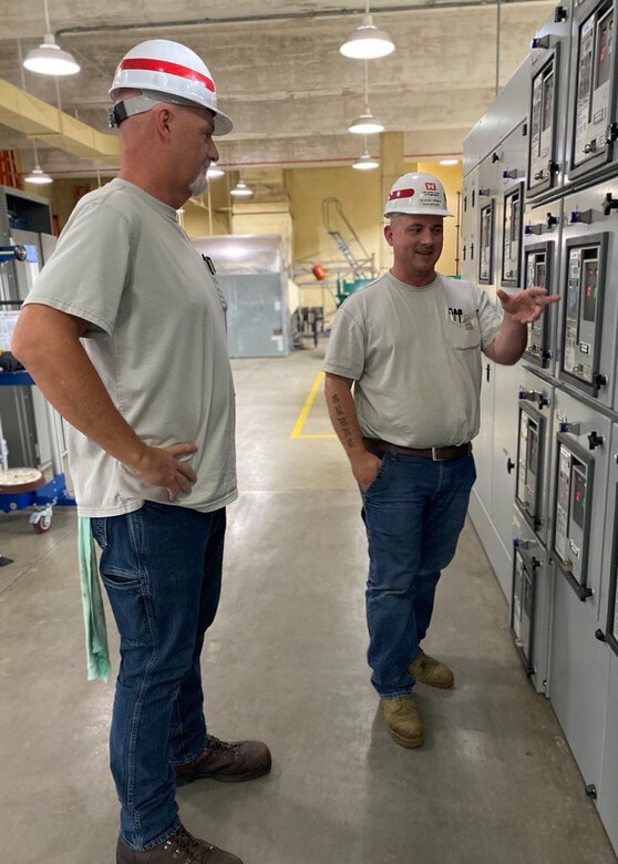 Two men stand in a control room and discuss transformers.