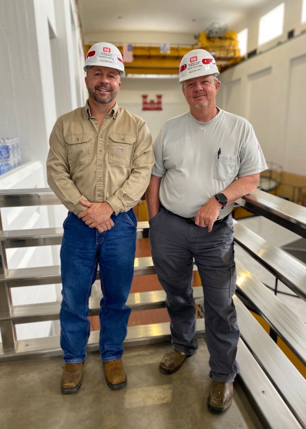 Two men stand in front of three generators.