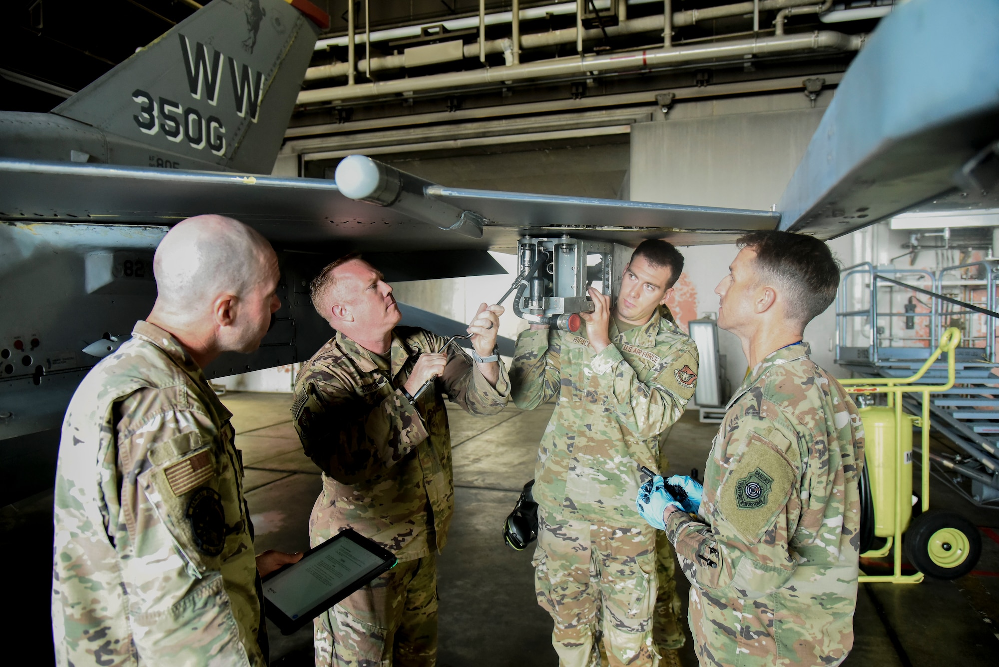 Service members attach a pylon to an F-16.