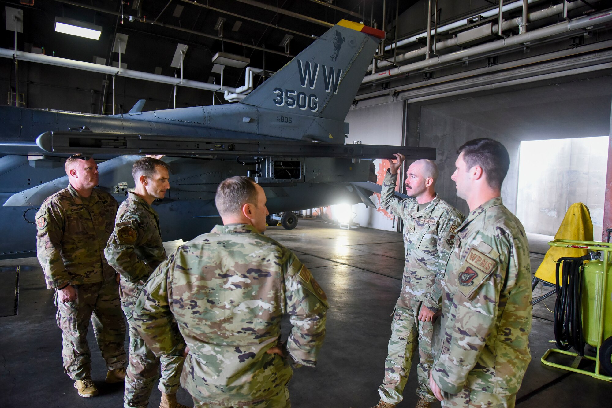 Service members stand around an F-16 talking