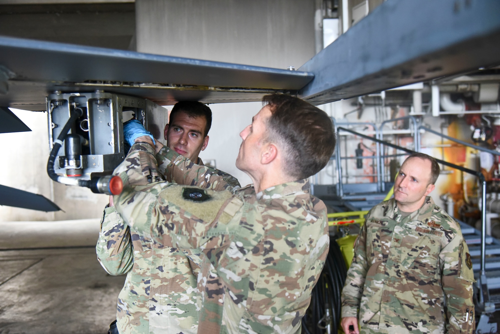 Service members attach a pylon to an F-16.