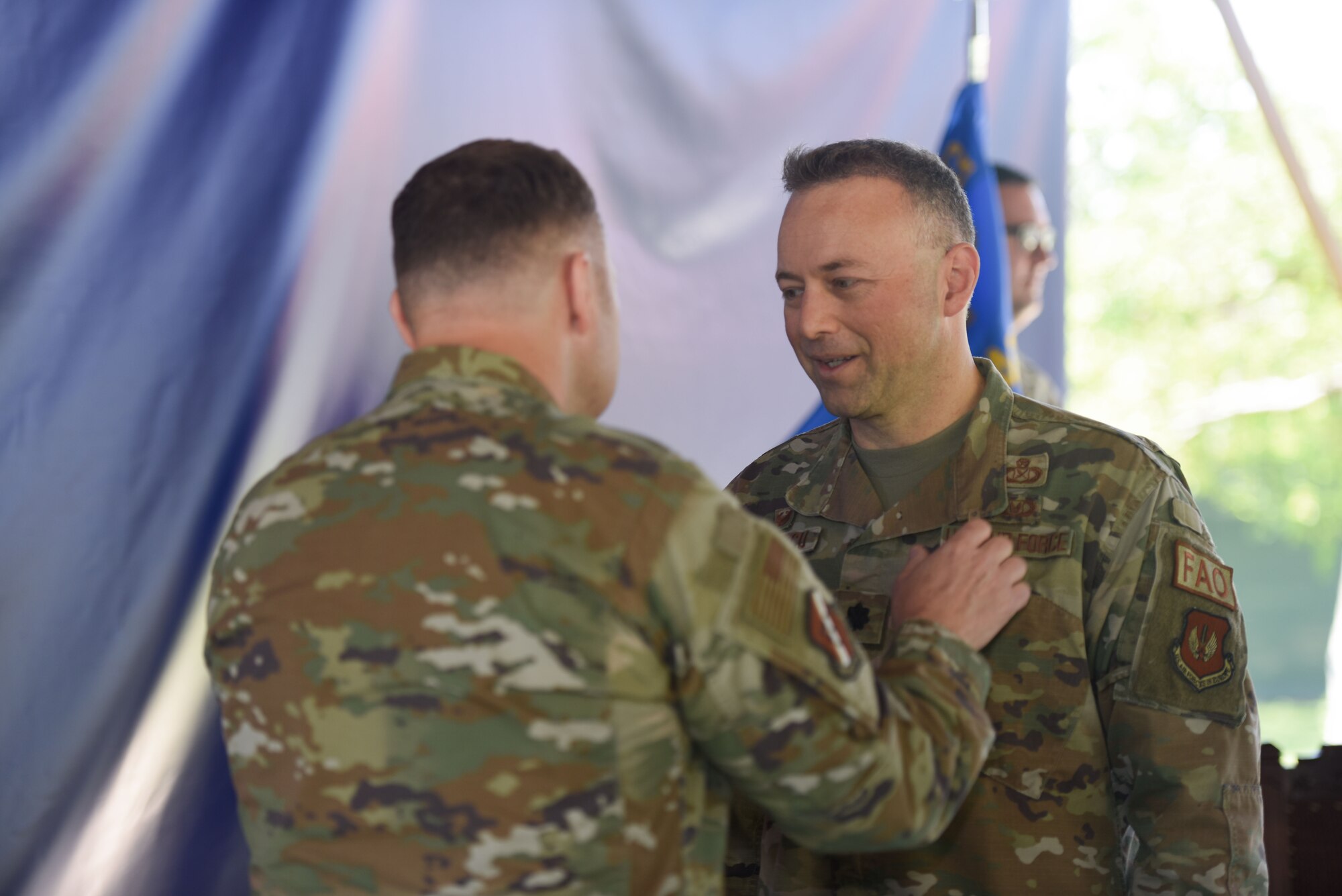 A man pins a medal onto the lapel area of another man's uniform.