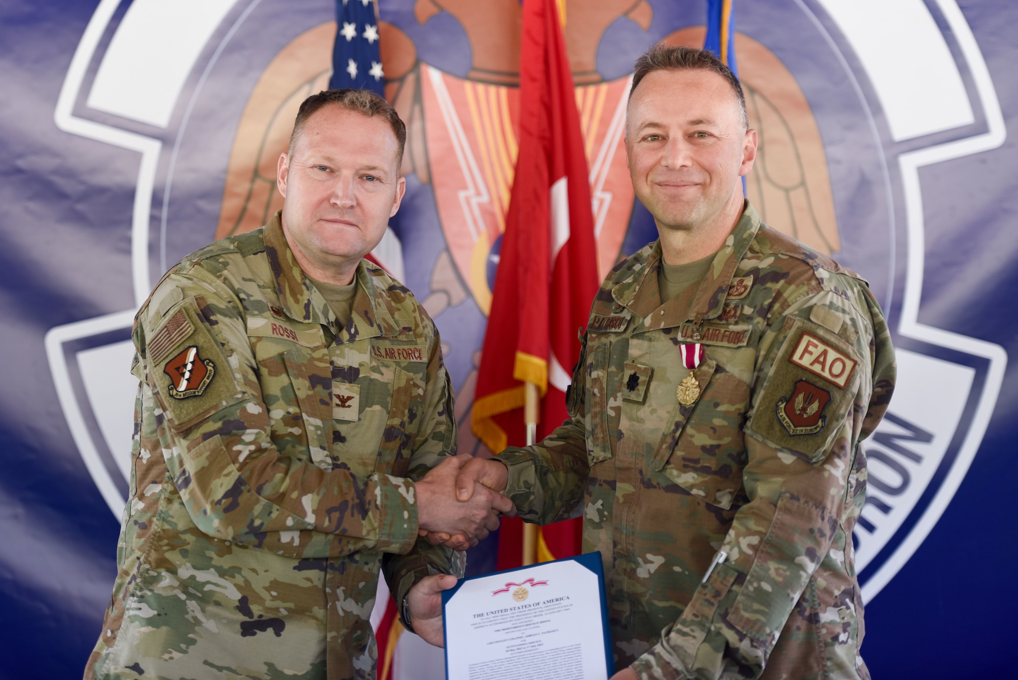 Two men shake hands while holding a document.