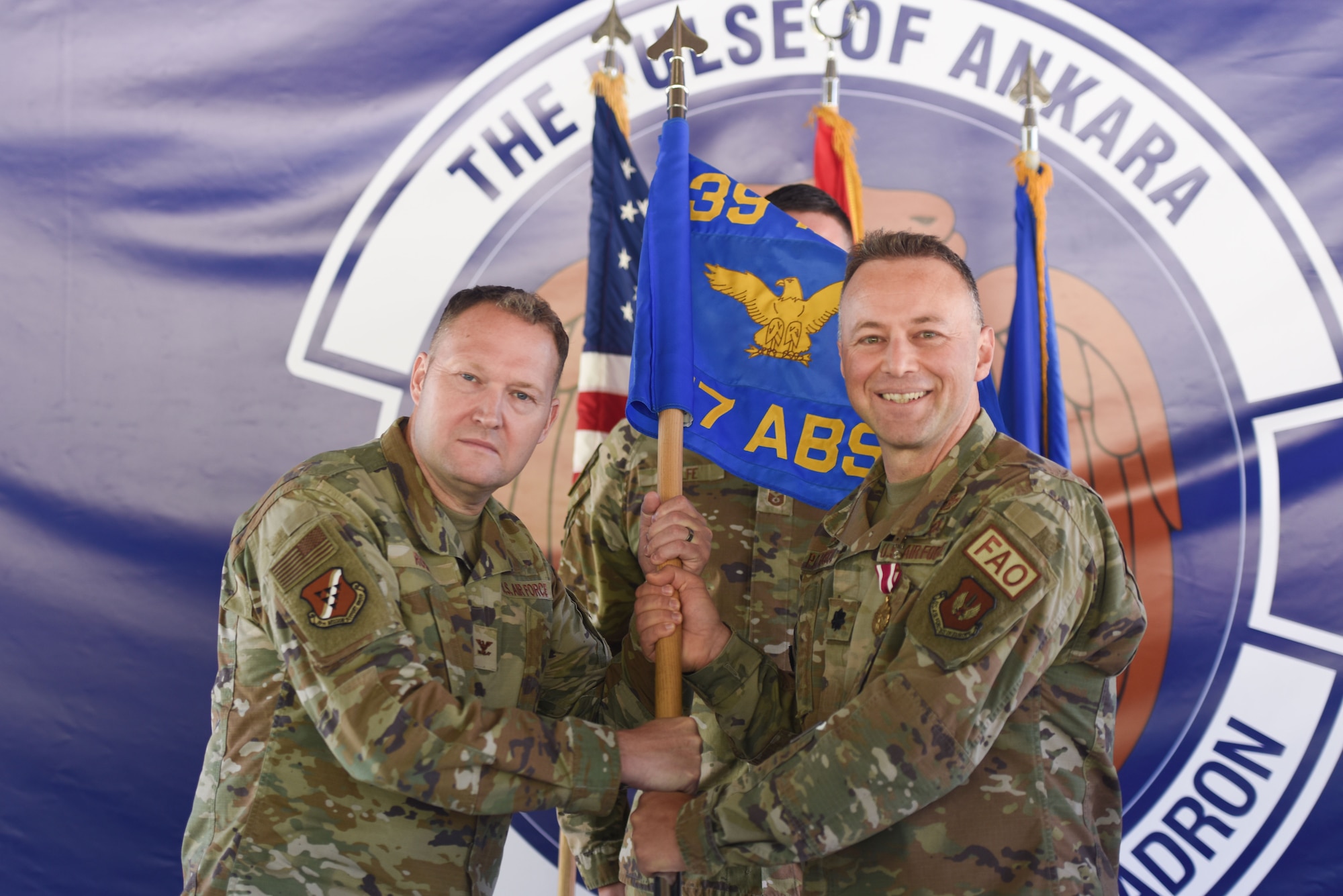 Two men in  U.S. Air Force uniforms hold a flag pole.