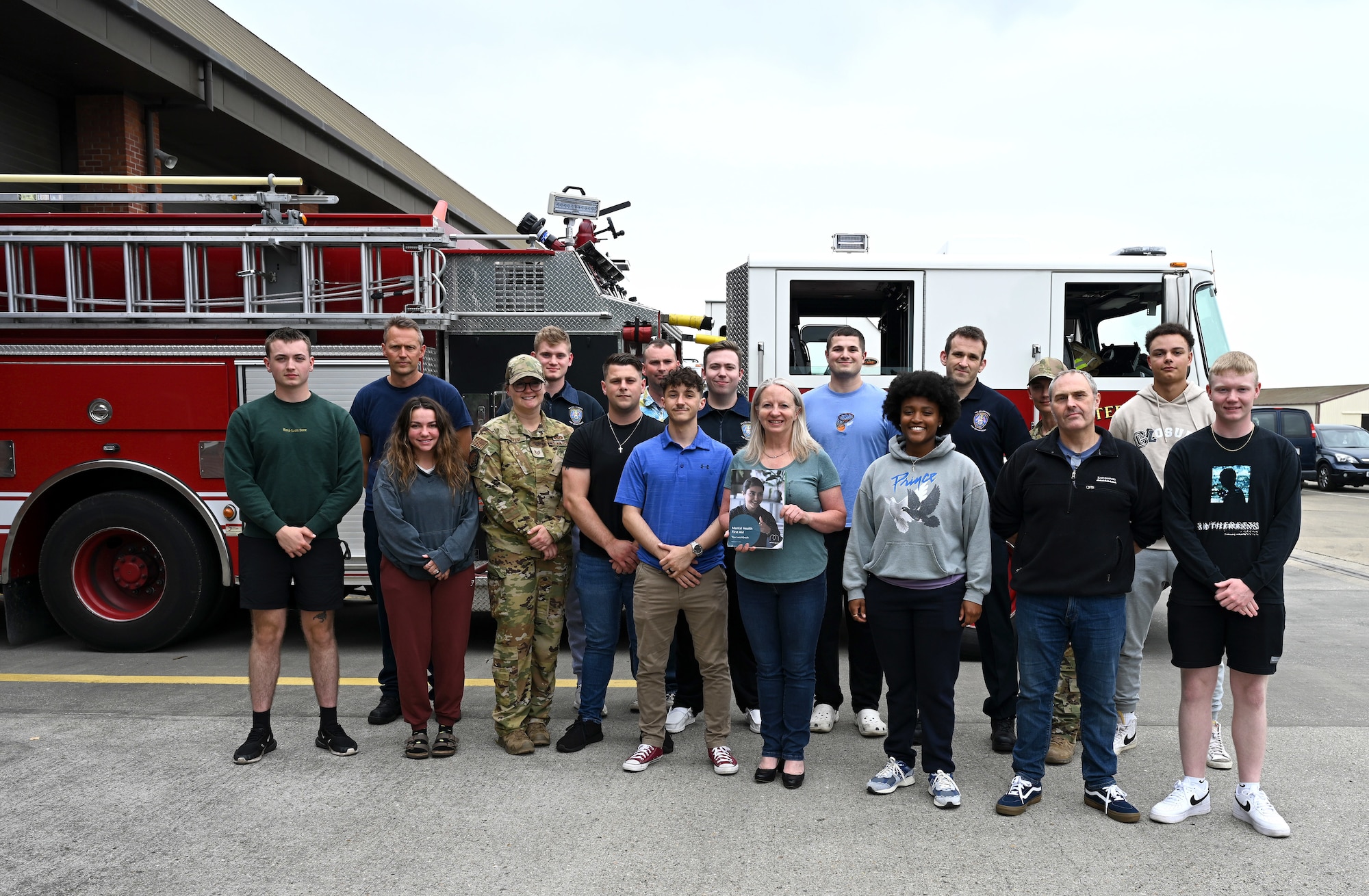 British civilians and U.S. Air Force Airmen from the 100th Civil Engineer Squadron Fire Department and 100th Security Forces Squadron, finish their two-day Mental Health First Aider course with a group photo with Maj. Pauline Murray-Knight MBE, center, MHFA national trainer, at Royal Air Force Mildenhall, England, June 27, 2023. First responders from both squadrons attended the training to help provide them the knowledge and confidence to help assist someone experiencing a mental health breakdown, challenge or crisis that they may be responding to or involved with. (U.S. Air Force photo by Karen Abeyasekere)