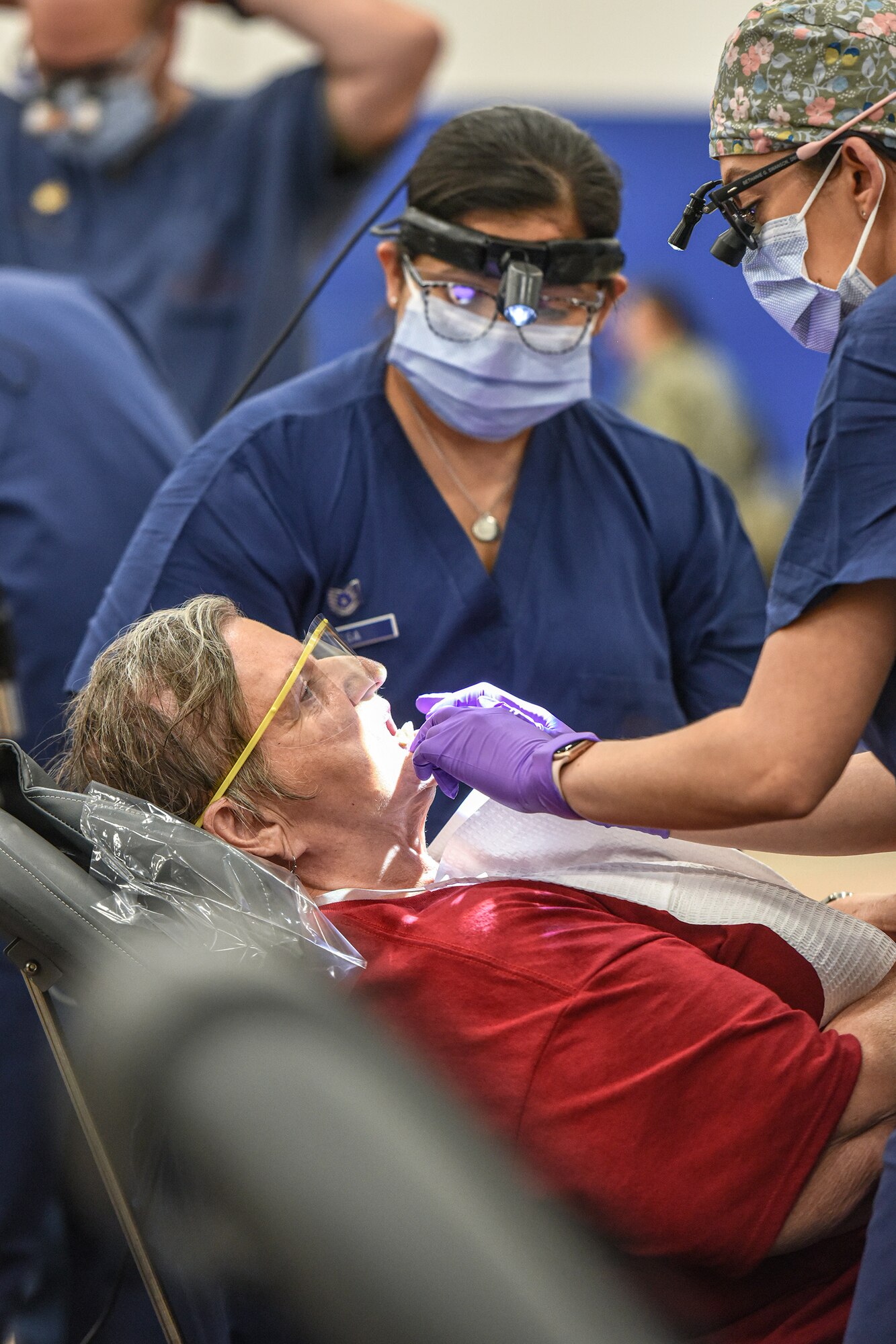 two dental workers provide care to a patient in a reclining dental chair.