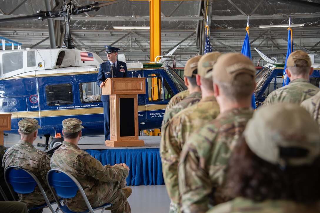 A crowd of military members listen to a man in a military dress uniform speak.