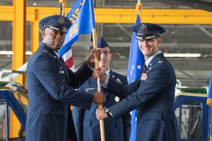 Two men in dress uniforms hold a flag.