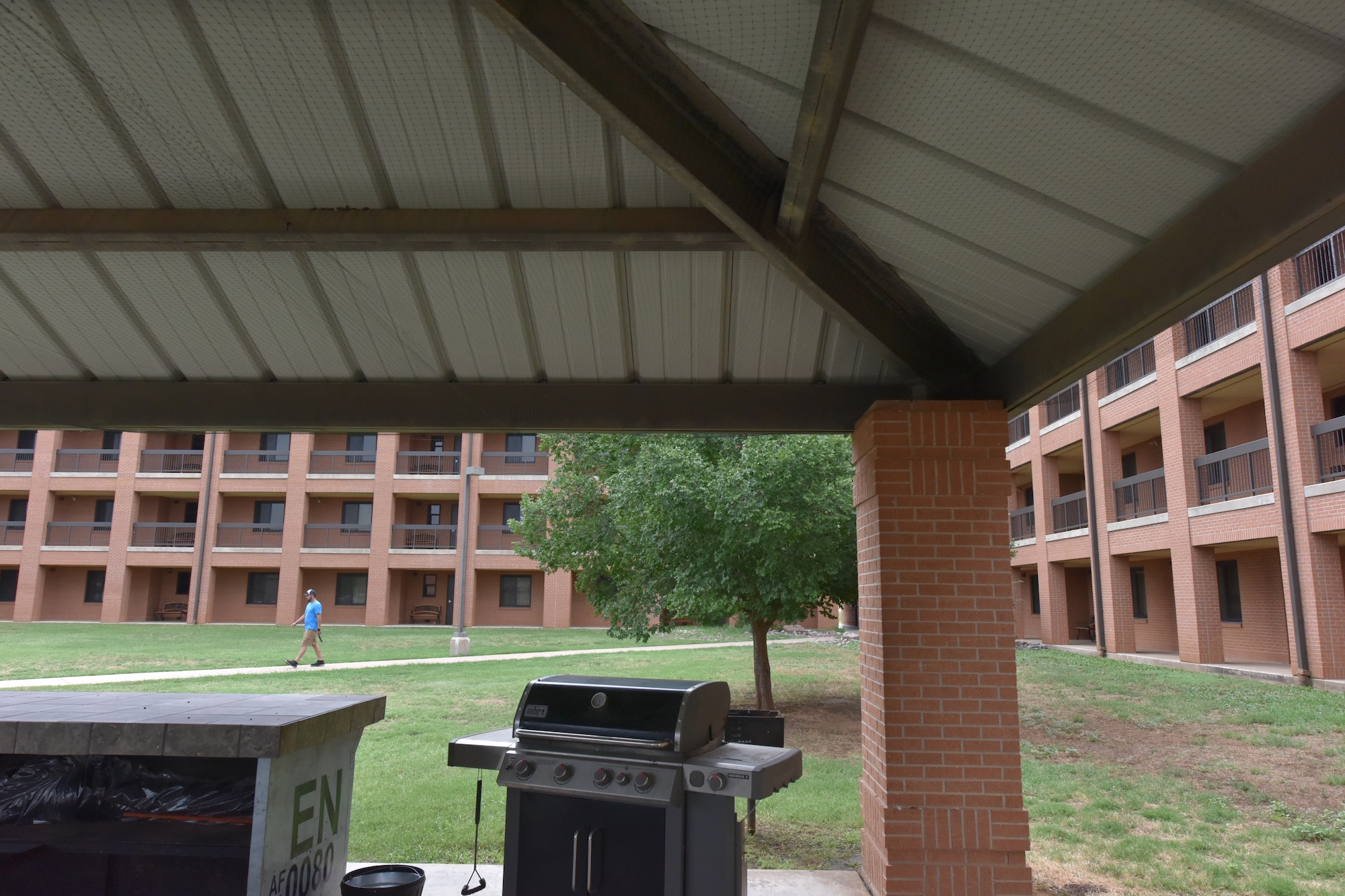 A grill is under bird netting in a brick gazebo outside a dorm building.