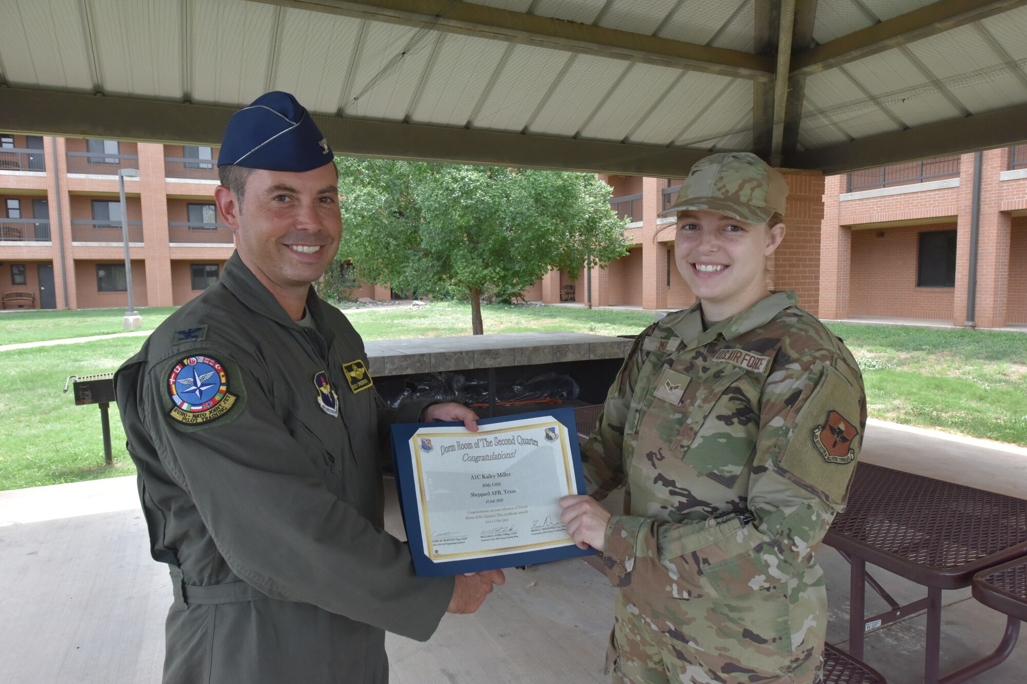 An Air Force Colonel handing a certificate to an A1C
