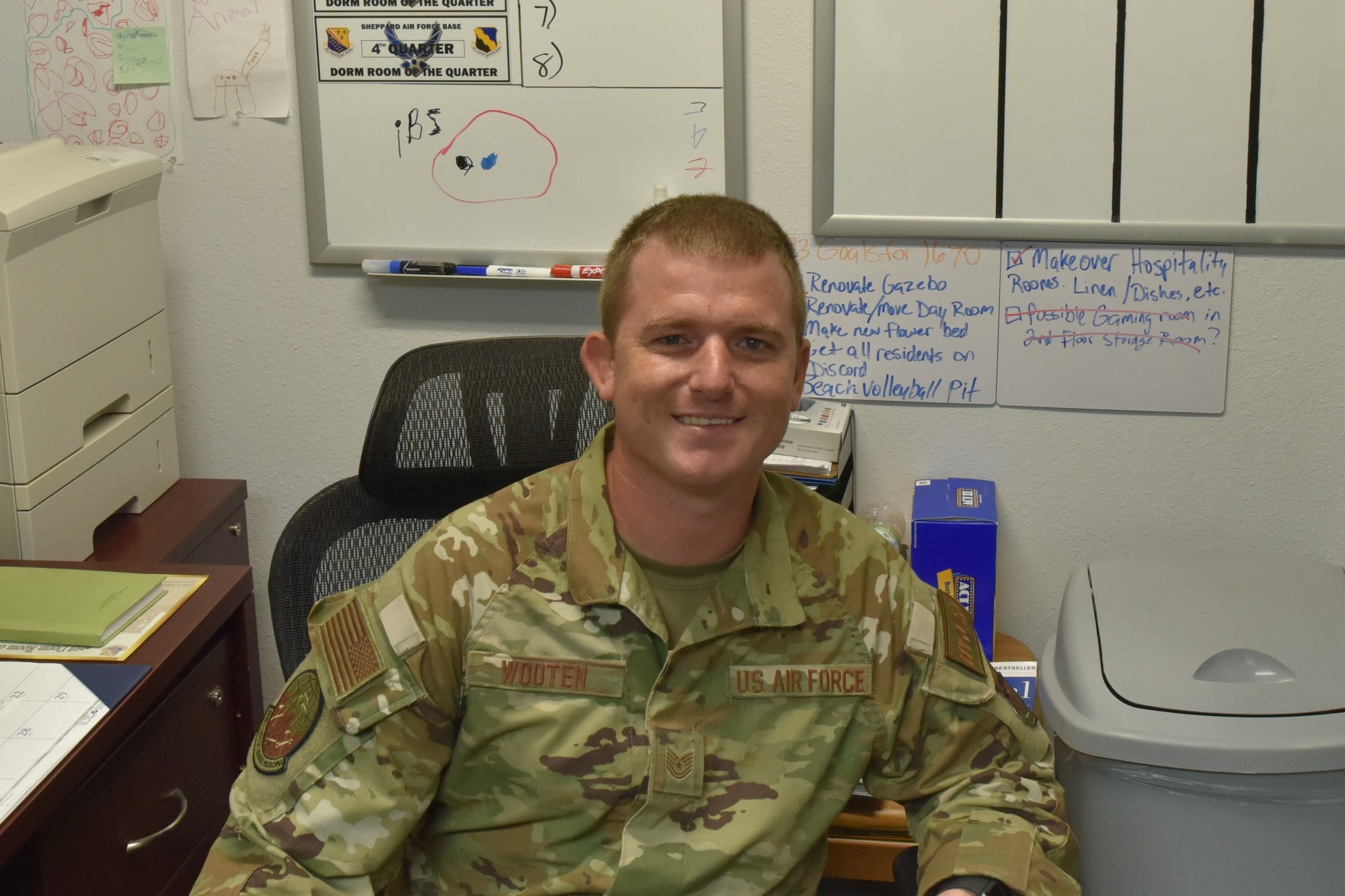 Air Force Tech Sgt. sits at desk in front of white board.