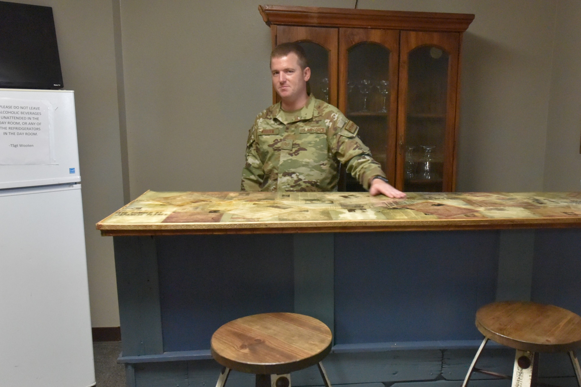 Air Force Tech Sgt stands behind a bar.