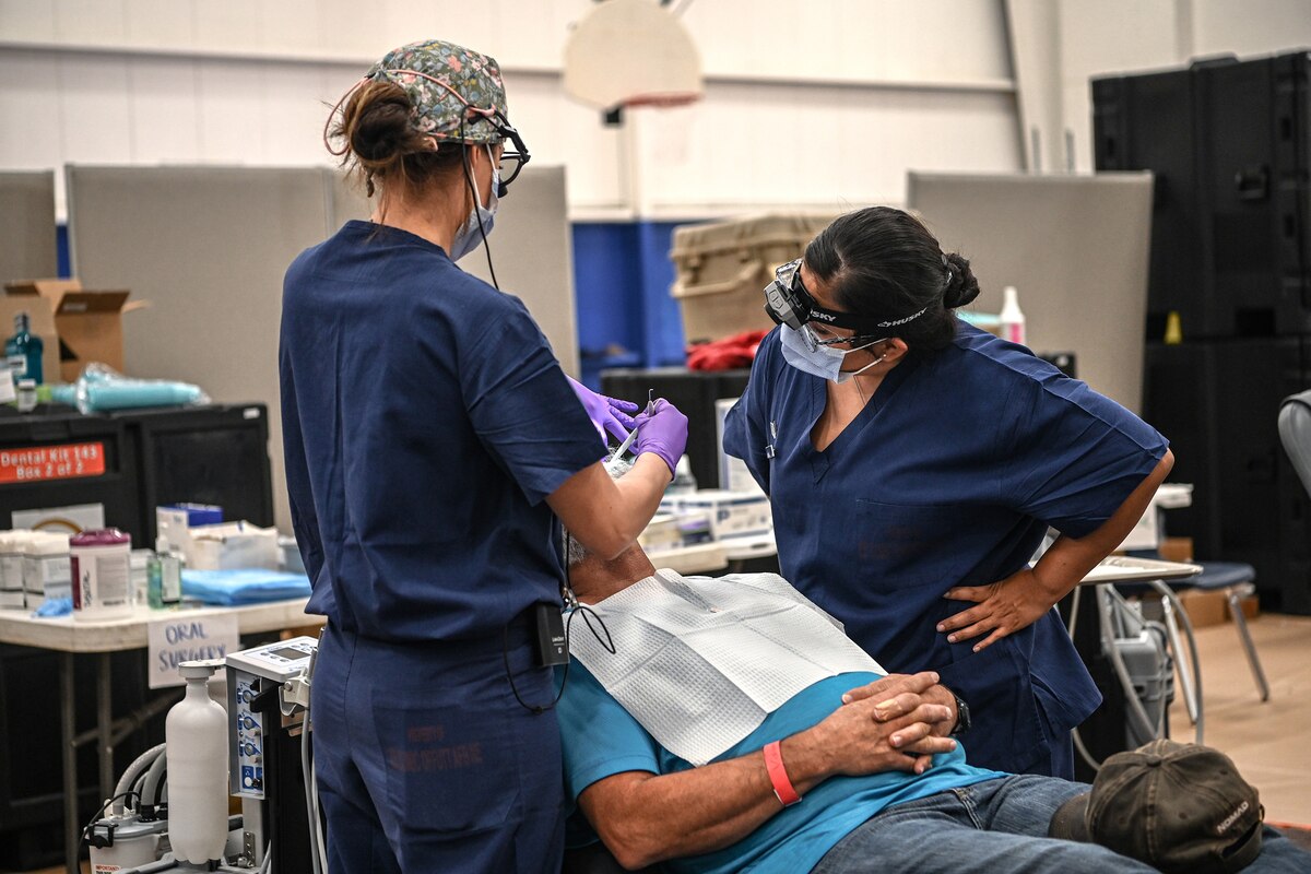Two dental workers administer care to a patient sitting in a dental chair.
