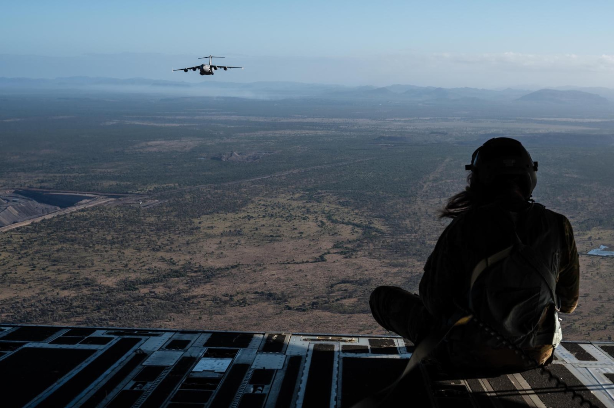 Royal Australian Air Force Corporal Charlotte Roe, a C-17 Globemaster III loadmaster assigned to No. 36 Squadron RAAF at Base Amberley, Australia, left, and U.S. Air Force Master Sgt. Jason Livingston, a C-17 loadmaster assigned to the 16th Airlift Squadron at Joint Base Charleston, South Carolina, right, watch as a U.S. C-17 from the 62nd Airlift Wing at Joint Base Lewis-McChord, Washington, flies behind a RAAF C-17 from No. 36 Squadron over the Commonwealth of the Northern Mariana Islands during Exercise Mobility Guardian 23 on July 12, 2023. MG23 is an opportunity to train alongside our Allies and partners to demonstrate interoperability and bolster our collective ability to support a free and open Indo-Pacific. (U.S. Air Force photo by Tech. Sgt. Sean Carnes)